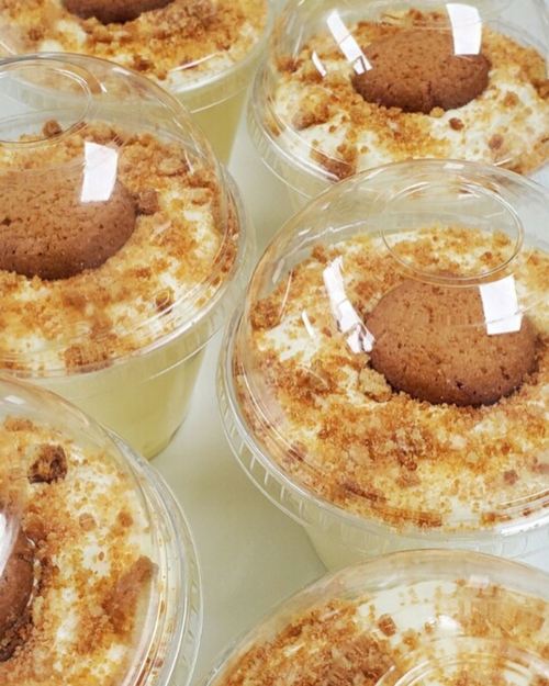 Six dessert cups filled with creamy layers, topped with crumbled cookies and a whole cookie on each.
