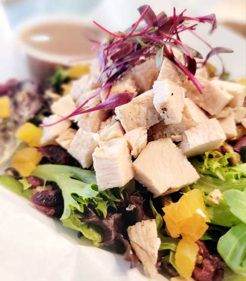 A fresh salad topped with diced chicken, mixed greens, and microgreens, served with a side of dressing.