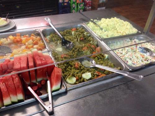 A buffet spread featuring watermelon, mixed fruit, green beans, scrambled eggs, and coleslaw in metal trays.