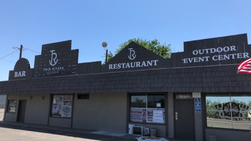 Signage for Twin Rivers Saloon, Restaurant, and Outdoor Event Center, with an American flag in the foreground.