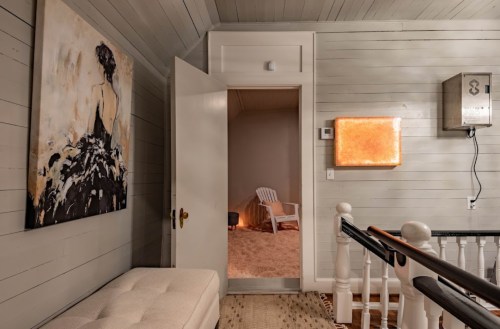 A hallway with a painting, an open door leading to a room, and a glowing wall art piece.