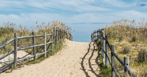 Sandy pathway leads to Sandbridge Beach in Virginia Beach, VA under a blue sky