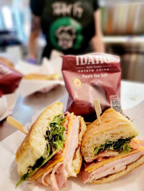 A close-up of a sandwich with turkey, cheese, and lettuce, alongside a bag of Idaho's Purple Sea Salt chips.