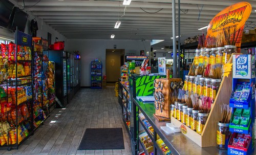 Interior of a convenience store featuring colorful snack displays, a checkout counter, and vending machines.