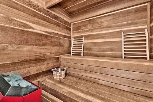 A wooden sauna interior featuring benches, a metal bucket, and a stone heater.
