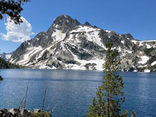 A serene mountain landscape featuring a snow-capped peak reflected in a clear blue lake, surrounded by trees.