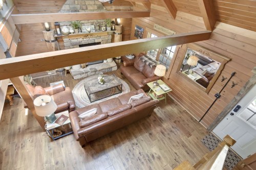 Cozy wooden cabin living room with leather sofas, a stone fireplace, and warm lighting.