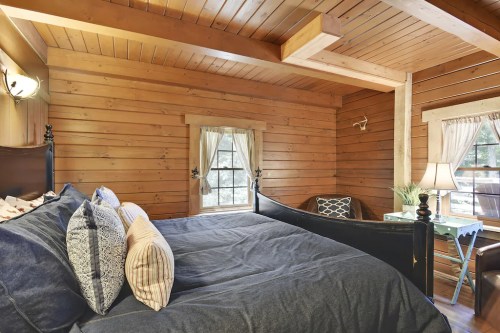 Cozy wooden bedroom with a large bed, decorative pillows, and a window with natural light.