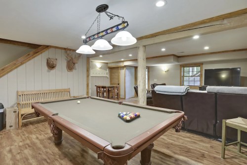 A cozy game room featuring a pool table, seating area, and warm lighting with wooden accents.