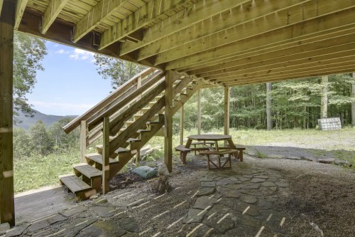 Wooden deck with stairs leading up, picnic table below, surrounded by trees and mountains in the background.