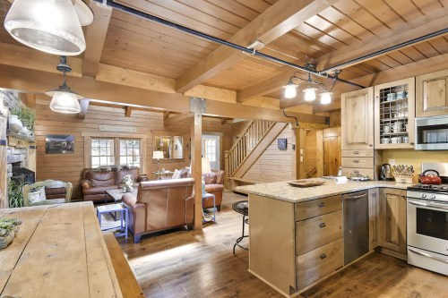 Cozy wooden kitchen with an island, stainless steel appliances, and a view of a rustic living area with leather sofas.