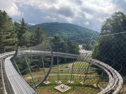 A winding roller coaster track surrounded by trees and mountains under a cloudy sky.