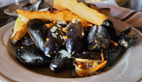 A plate of mussels topped with orange and white garnishes, accompanied by crispy fries.