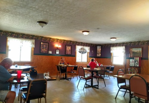 A cozy restaurant interior with wooden decor, featuring two patrons at separate tables and bright windows.
