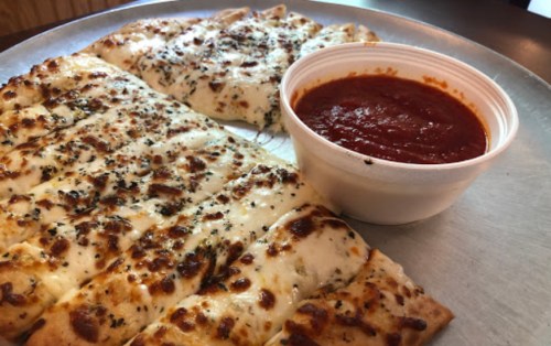 A plate of cheesy garlic breadsticks with a side of marinara sauce.
