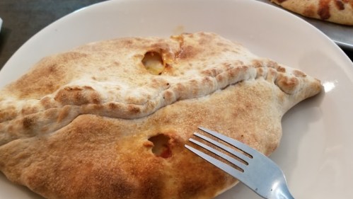 A golden-brown calzone on a white plate, with a fork resting beside it.