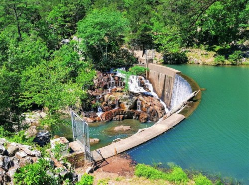 A serene landscape featuring a small waterfall cascading into a green lake, surrounded by lush trees and rocks.
