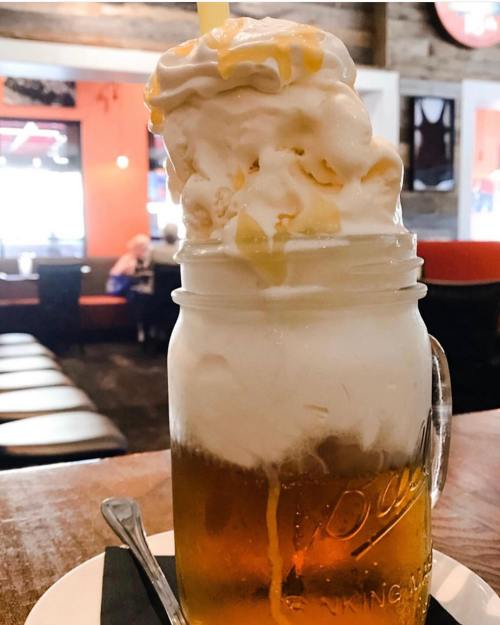 A mason jar filled with beer topped with a large swirl of creamy ice cream and drizzled with syrup.