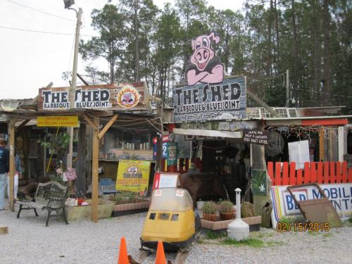 A rustic barbecue joint with colorful signs, outdoor seating, and a playful pig logo, surrounded by trees.