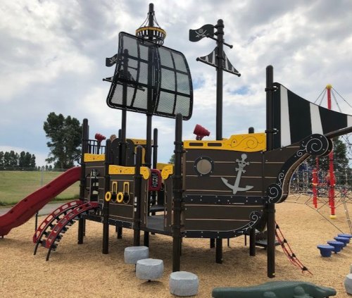 A colorful pirate ship-themed playground with slides, climbing features, and a flag, set in a grassy area.