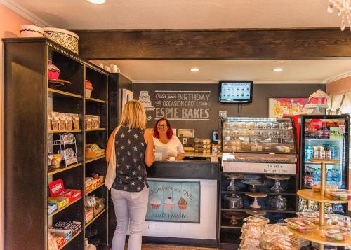 A customer interacts with a baker at a cozy bakery, surrounded by shelves of treats and a display case of desserts.