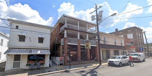 A street view of a brick building with balconies, flanked by two smaller structures, under a blue sky with clouds.