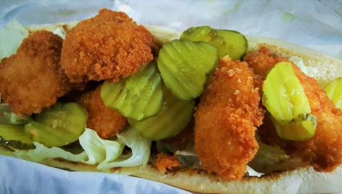 A sandwich filled with crispy fried chicken pieces, pickles, and lettuce on a soft bun.