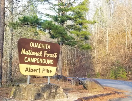 Sign for Ouachita National Forest Campground, Albert Pike, surrounded by trees and rocky terrain.