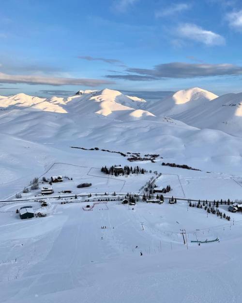 A snowy landscape with rolling hills, a ski slope, and a small village under a clear blue sky.