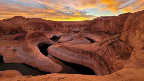 A stunning sunset over a winding river surrounded by red rock formations and dramatic clouds in the sky.