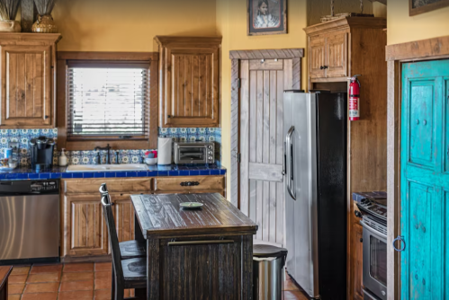 Cozy kitchen with wooden cabinets, blue tile backsplash, stainless steel appliances, and a rustic dining table.