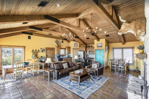 Spacious rustic living room with wooden beams, yellow walls, and a cozy seating area, featuring a dining space and decor.
