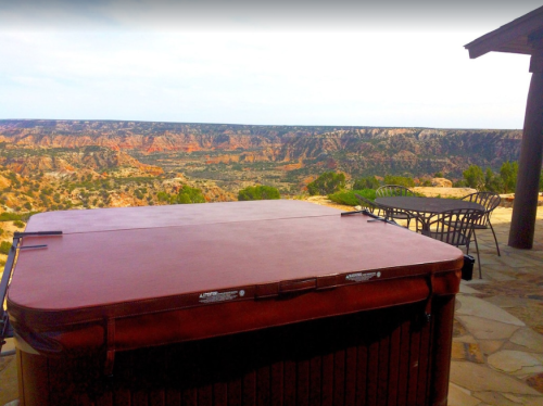 A hot tub on a patio overlooking a scenic canyon landscape with colorful rock formations and distant hills.