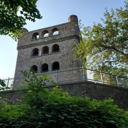 A stone tower with arched windows, surrounded by greenery and a clear blue sky.