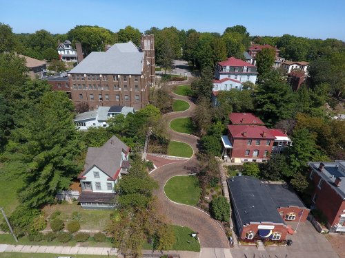 Aerial view of a winding street lined with trees and various residential buildings in a suburban area.