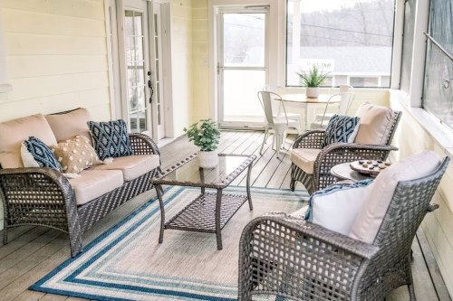 Cozy porch with wicker furniture, cushions, a glass table, and a small dining set, surrounded by light-colored walls.