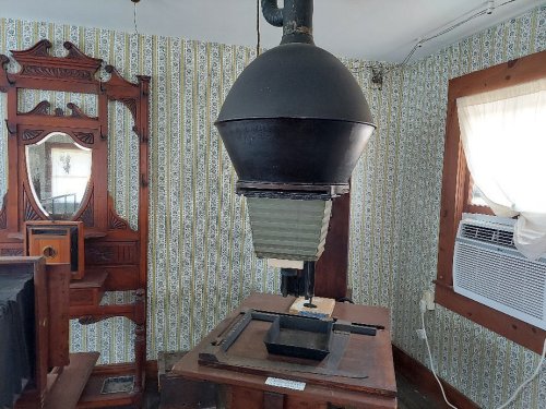 A vintage printing press in a room with patterned wallpaper and a mirror, showcasing historical craftsmanship.