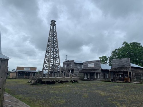 A rustic old western town with wooden buildings and a tall oil derrick under a cloudy sky.
