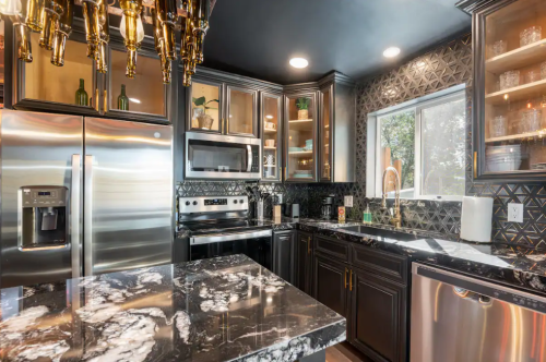 Modern kitchen featuring dark cabinets, marble countertops, stainless steel appliances, and stylish lighting.