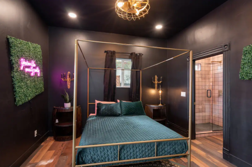 A stylish bedroom with a four-poster bed, dark walls, greenery accents, and a modern shower in the background.