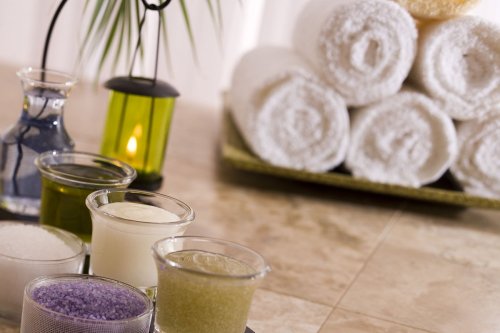 A spa setting with various scented oils and salts in glass containers, alongside neatly rolled white towels and a candle.
