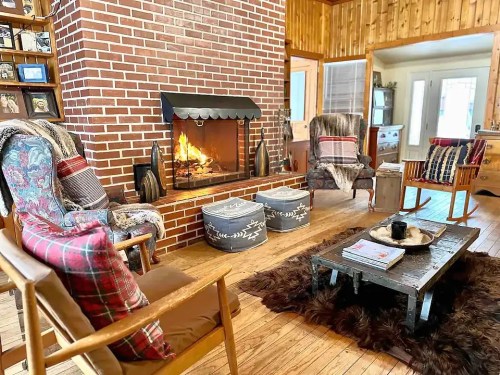 Cozy living room with a brick fireplace, comfortable chairs, a wooden coffee table, and warm decor.