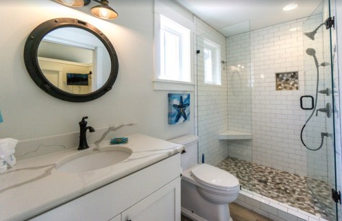 Modern bathroom featuring a glass shower, white tiles, a round mirror, and a stylish sink with a marble countertop.