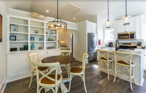 Bright kitchen with white cabinetry, a round table, and modern appliances, featuring pendant lighting and a cozy atmosphere.