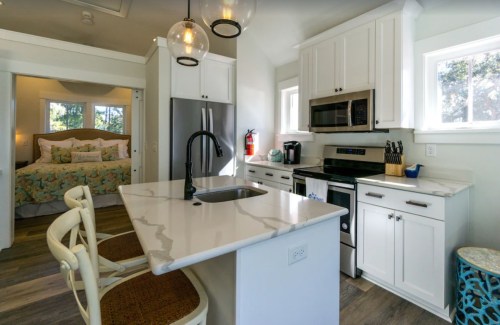 Modern kitchen with white cabinets, stainless steel appliances, and a marble countertop, adjacent to a cozy bedroom.