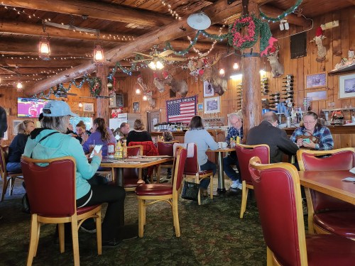 A cozy restaurant interior with wooden decor, patrons dining, and festive decorations.
