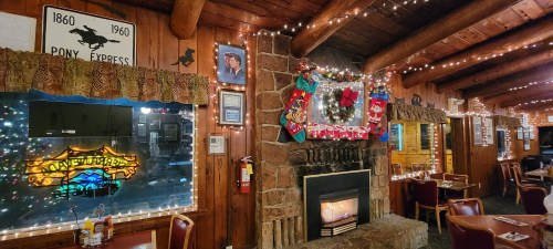 Cozy restaurant interior decorated with holiday lights, a fireplace, and festive ornaments on wooden walls.