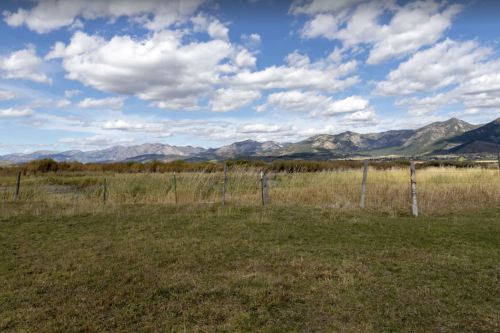 A scenic landscape featuring rolling hills, a grassy field, and a cloudy sky with distant mountains.