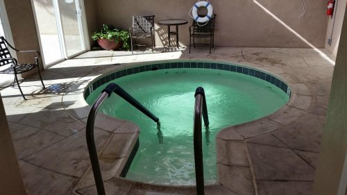 A small, circular hot tub with steps, surrounded by a patio area and chairs, in a well-lit indoor space.