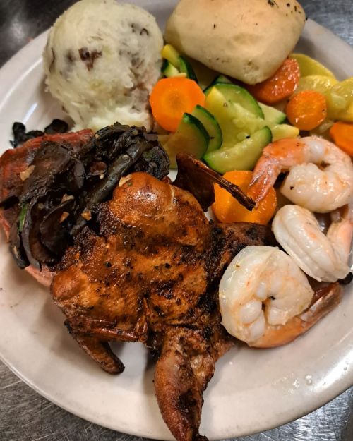 A plate featuring grilled chicken, shrimp, mashed potatoes, and mixed vegetables including carrots and zucchini.